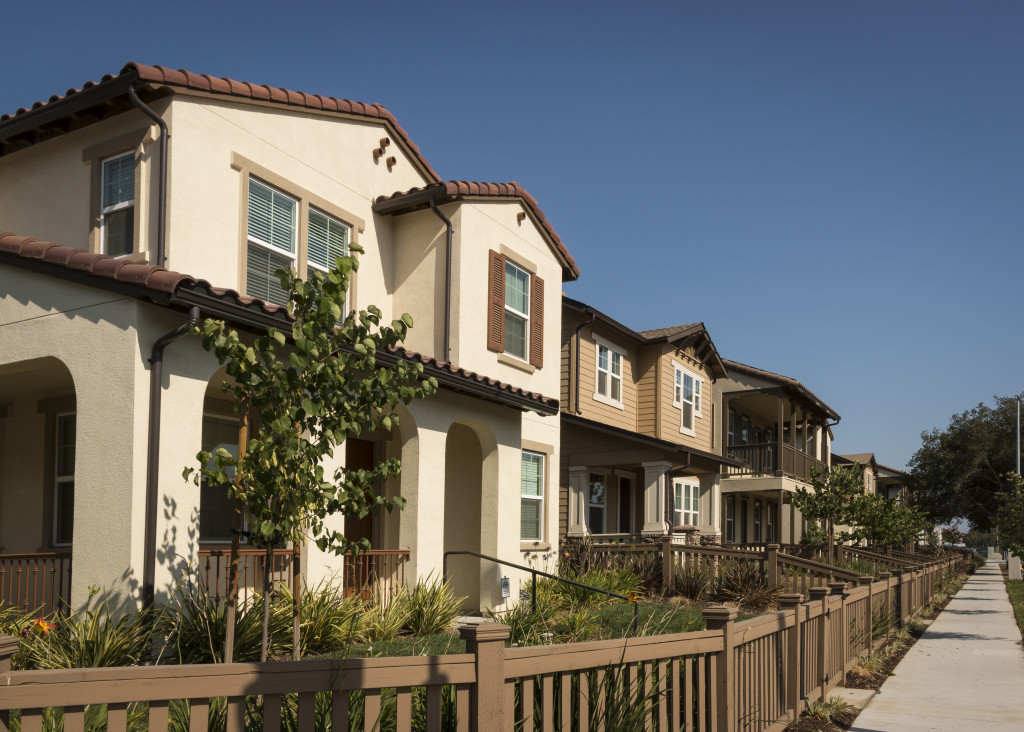 A row of new homes with fenced yards along a sidewalk.