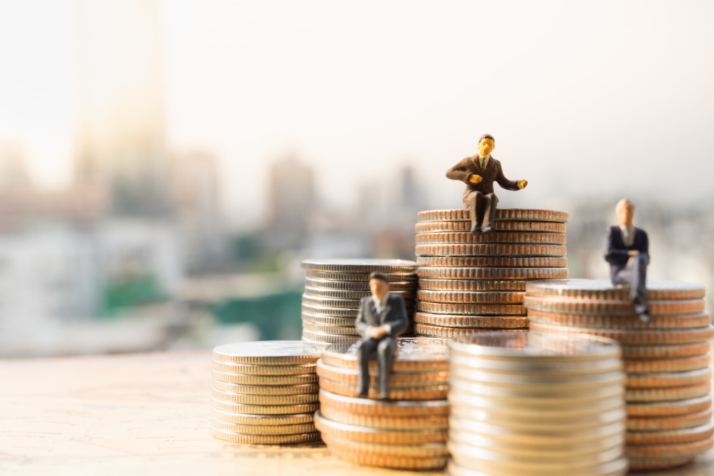 Miniature businessmen sitting on stacks of coins