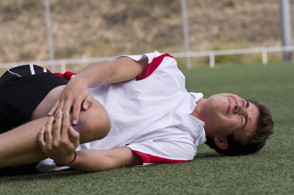 Injured football player holding his knee during practice.