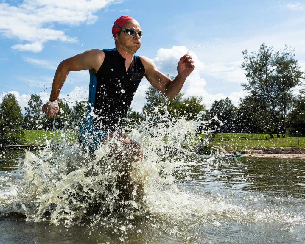 Male triathlete running out of the water to the next stage.